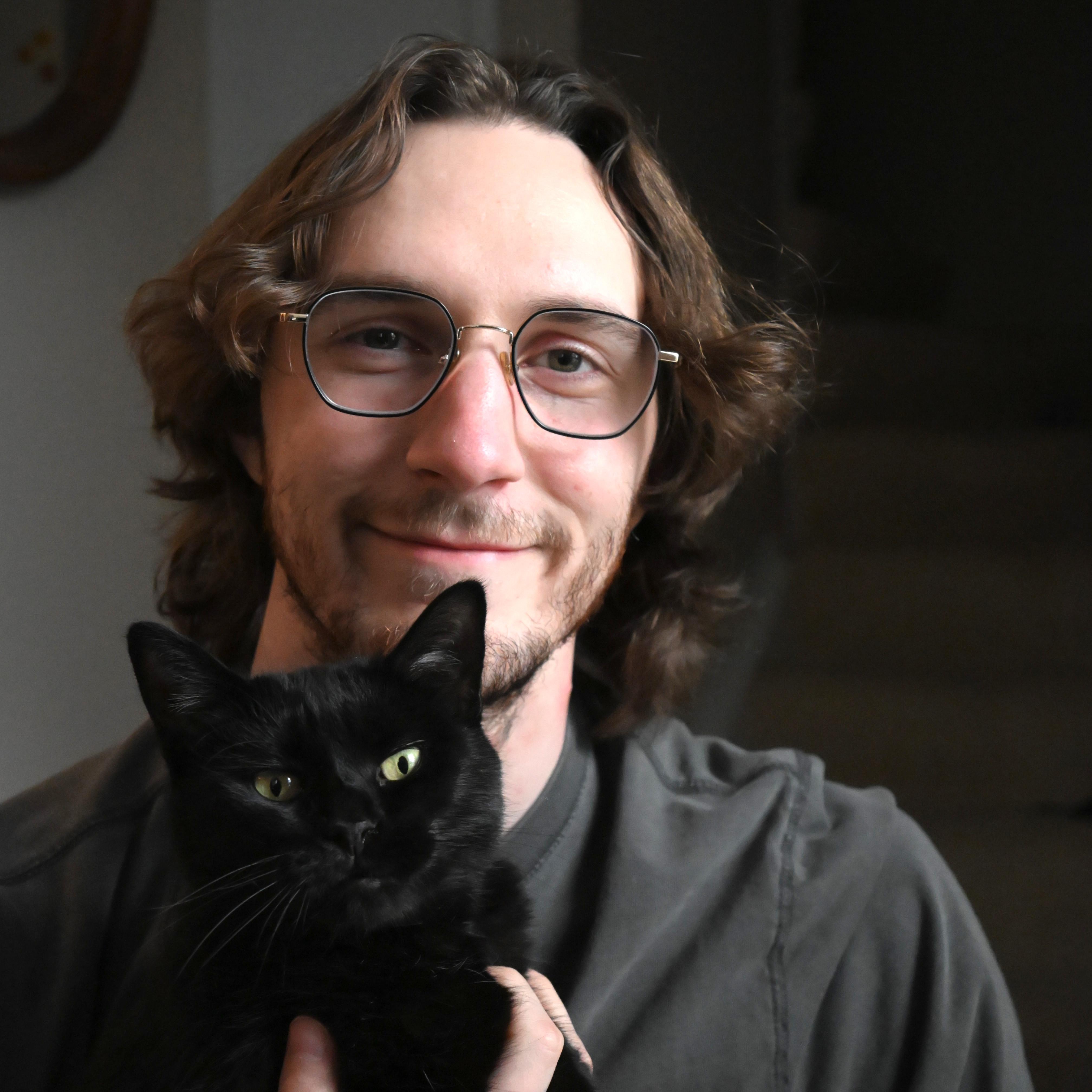 A portrait of me smiling and holding my black short-hair cat, Marby